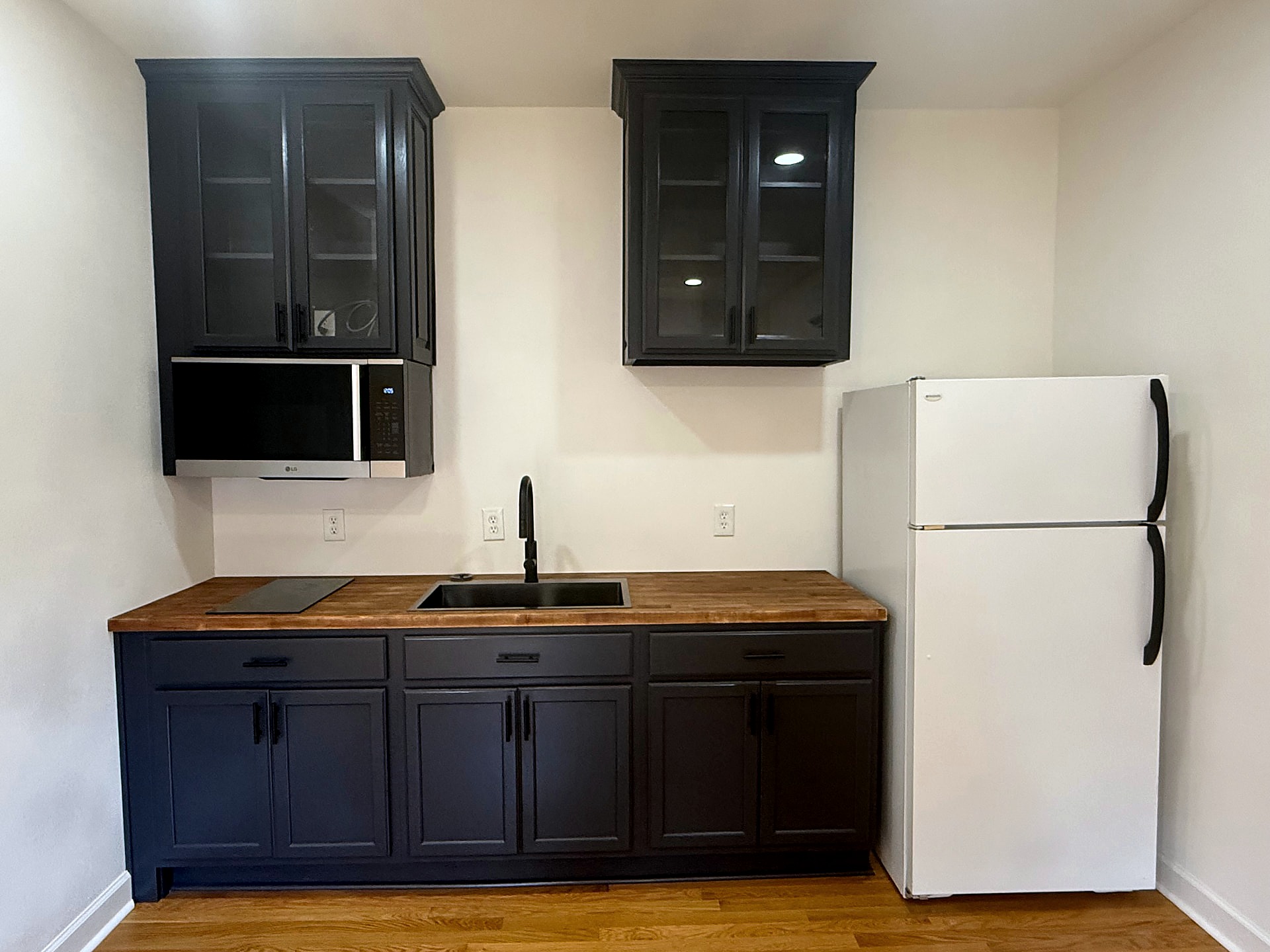 Carriage-house studio kitchenette with black cabinetry and wood countertop